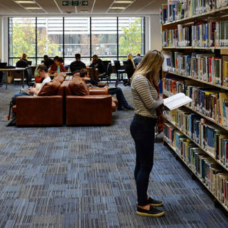 female student standing and reading by the bookshelves in the Ƶ Library
